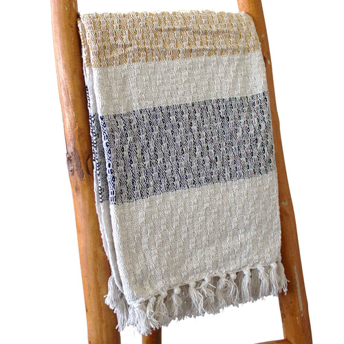 Textured blanket with fringes draped over a wooden ladder on a white background